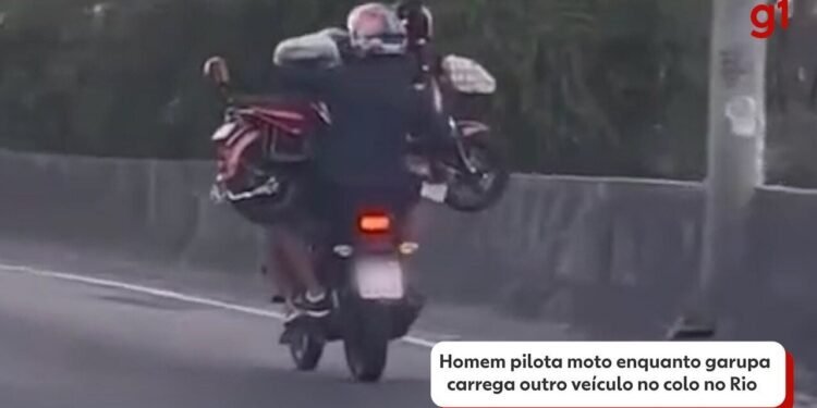 Homem piloto de moto enquanto garupa carrega outro veículo no colo na Barra da Tijuca; VÍDEO